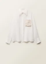 Camisa blanca de ramio con cuello camisero, cierre frontal con botones, bolsillo de parche con detalle bordado y mangas largas abotonadas.