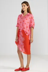 Camisa de manga larga color rosa con rayas verticales rojas y estampado de flores rojas. Tiene cuello camisero, puños elastizados y lazos regulables en los costados del ruedo.