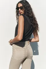 Pantalón de jean color beige, de tiro alto, corte ajustado en la cadera y muslos, y acampanado desde la rodilla. Tiene cinco bolsillos y cierre frontal con cremallera y botón.