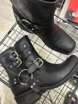 Bota negra de corte bajo con detalles de hebillas y anillo, diseño robusto.