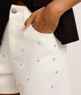 Short de cintura alta en sarga color blanco, con trabillas en la cintura, cierre tradicional, bolsillos, lunares de metal y strass aplicados.