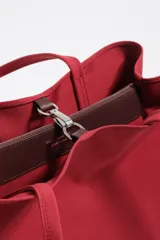 Bolso shopper grande de nylon negro, con estructura blanda, doble asa de mano y correa larga ajustable para llevar al hombro. Presenta un logo metálico con el texto "BIMBA Y LOLA" en la parte frontal inferior.