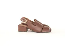 Sandalia de cuero color marrón con punta cuadrada y tiras anchas entrecruzadas. Tiene talón abierto con pulsera ajustable y hebilla metálica. El taco es ancho y mide 4 cm.