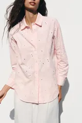 Camisa manga larga color rosa pálido con cuello solapa y cierre frontal con botones. Detalle de bordados perforados engomados con motivos florales. Corte recto.