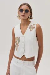 Chaleco blanco de gabardina con bordados florales y cierre frontal con botones forrados en la misma tela.