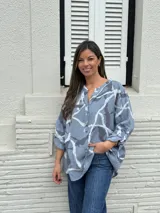 Camisa celeste con estampado batik en tonos grises y blancos, cuello mao con botones y mangas 3/4 con trabilla.