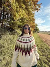 Sweater de lana color crudo con cuello alto y diseño geométrico en tonos verde y bordó.