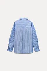 Camisa celeste con rayas verticales blancas, de corte holgado, cuello solapa, escote en pico y mangas largas con puños abotonados.