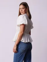 Blusa blanca de algodón con bordado broderie, escote en V con abertura central y botones, cintura elastizada y mangas cortas con terminación elastizada.