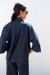 Camisa de denim azul con cuello de solapa, escote en pico, cierre frontal con botones y mangas anchas hasta el codo.