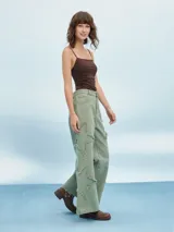Pantalón de jean verde con corte acampanado y múltiples roturas con flecos.