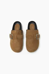 Zueco color beige con hebilla metálica ajustable, confeccionado en material símil gamuza y suela de goma negra.