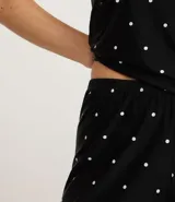 Pijama short doll femenino compuesto por una musculosa y un short. La musculosa es de breteles finos ajustables, escote en V con detalle de encaje cruzado en el busto. El short es corto con cintura elástica. Estampado de lunares blancos sobre fondo negro.