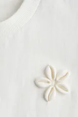 Remera blanca de algodón con cuello redondo y apliques de flores en el frente.