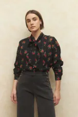 Camisa color crema con estampado de rosas rojas y amarillas, de manga larga y confeccionada en gasa. Tiene cuello con lazo y botones de nácar.