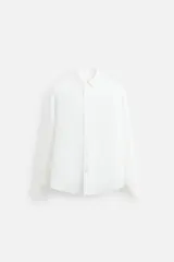 Camisa blanca de lino, corte regular fit, cuello abotonado, manga larga con puños abotonados, pliegue en la espalda, bajo con aberturas laterales y cierre frontal con botones.