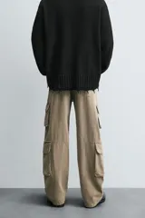 Pantalón de denim color beige, corte relaxed fit, con bolsillos laterales tipo cargo con solapa y cierre de botón. Cierre frontal con botón y cremallera.