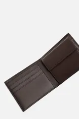 Billetera tipo cartera fabricada en piel color marrón oscuro. Cuenta con un compartimento para billetes, tres compartimentos para tarjetas, dos ranuras laterales y un monedero con cierre mediante clip.