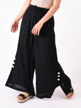 Pantalón palazzo negro con cintura elástica y cordón ajustable. Presenta aberturas laterales con botones blancos.