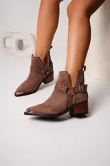 Botas texanas cortas de cuero color marrón con puntera metálica, detalles de tachas y arnés con hebilla. Taco de madera.