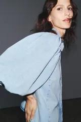 Blusa de denim celeste con cuello solapa y mangas abullonadas por debajo del codo. Cierre frontal con botones.