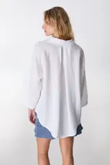 Camisa de lino color blanco, de manga larga y corte holgado, con cuello camisero y cierre frontal de botones.