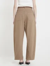 Pantalón color café de gabardina, corte relajado, con pinzas sutiles, bolsillos delanteros, cintura con presillas y cinturón de cuero fino con flecos.