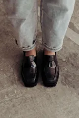 Zueco negro con textura croco, diseño tipo mocasín y tira regulable al talón.