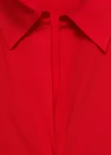 Camisa roja de tejido fluido con cuello camisero, cierre frontal con botones, mangas largas con puños abotonados y aberturas laterales.