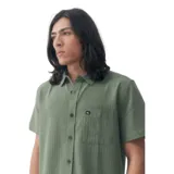 Camisa verde de manga corta con textura, cuello clásico, cierre con botones marrones y bolsillo en el pecho con logo de la marca.