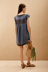 Vestido corto azul denim con bordados en hilo negro en escote, mangas y ruedo. Corte amplio y bolsillos laterales ocultos.