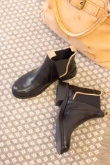 Botas Chelsea negras de cuero con elástico lateral y tirador trasero en color tostado. El talón tiene un detalle de cuero texturizado.