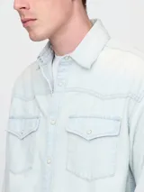 Camisa de jean celeste de manga larga con dos bolsillos frontales con solapa abotonada.