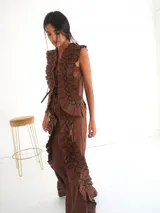 Top negro sin mangas, con escote en V profundo y detalle de apliques de tela fruncida o plisada en el frente y hombros. Se ata en el centro delantero con cintas.