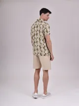 Camisa de manga corta con estampado de hojas color verde sobre fondo beige, cuello solapa y bolsillo en el pecho.