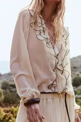 Camisa color crema de manga larga con escote en pico y volantes negros en el frente.
