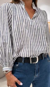 Blusa celeste y blanca a rayas verticales, de manga larga con puños abotonados, escote en pico con cuello ruffle y cierre delantero con botón.