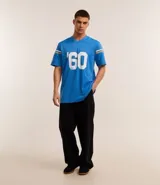 Remera deportiva azul con cuello en V y mangas cortas con rayas blancas y doradas. Estampado frontal con el logo de Los Angeles Chargers, el número 60 y la inscripción "est.". Confeccionada con tecnología Dry para mayor transpirabilidad.