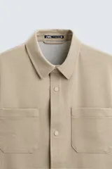 Sobrecamisa negra de tejido con elasticidad, cuello solapa, manga larga con puño abotonado, bolsillos de plastrón en el pecho y cierre frontal con botones a presión.