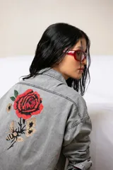 Camisa oversize de jean gris con bordado de una rosa roja, flores y una abeja en la espalda.