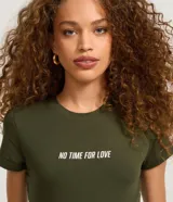 Blusa baby look verde militar de algodón con elastano, cuello redondo, mangas cortas y estampado frontal con la frase "No Time For Love" en color blanco.