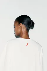 Camiseta blanca de algodón con cuello redondo, mangas cortas y hombros caídos. Estampado frontal con el título de la película "El Diablo Viste de Prada" en letras rojas.
