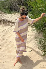 Vestido tejido artesanalmente en hilado 70% algodón y 30% acrílico, con cuello redondo y mangas cortas. Diseño a rayas horizontales en tonos crudo, naranja y beige. Corte recto con aberturas laterales en el ruedo.