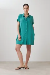 Túnica verde de lyocell con cuello camisero, manga corta con dobladillo y cierre frontal con botones.