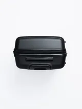 Valija rígida de viaje color negro con diseño de líneas horizontales en relieve. Cuenta con manija retráctil, cuatro ruedas con giro de 360°, candado de seguridad y organizadores internos.