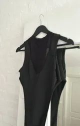 Body negro con cuello redondo, sin mangas y corte cavado. Presenta paneles de tela opaca en el centro y laterales, y paneles de tela transparente en el frente y laterales.