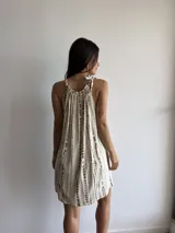 Vestido corto color crudo con estampado de líneas verticales marrones, cuello redondo con frunce y tirantes con lazo.