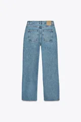 Jeans tobilleros de tiro alto color blanco, corte recto y bajo sin costura. Cierre frontal cruzado con cremallera y botones.