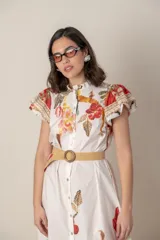 Vestido midi camisero de algodón color natural con estampado de flores, animales y ramas en tonos rojo, marrón, verde y azul. Tiene cuello mao, mangas cortas con volados, bolsillos laterales y cinturón de soga color beige.