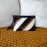 Sobre de mano de símil cuero con diseño de franjas diagonales en negro, blanco y marrón. Cuenta con cierre metálico frontal, bolsillo interior con cierre y otro abierto con división. Incluye correa desmontable para usar como bandolera.